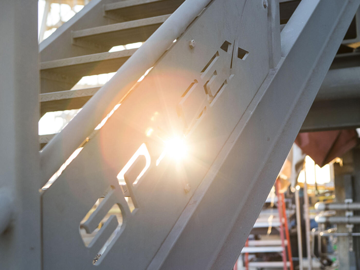 A railing with the sun shining through the SpaceX logo 