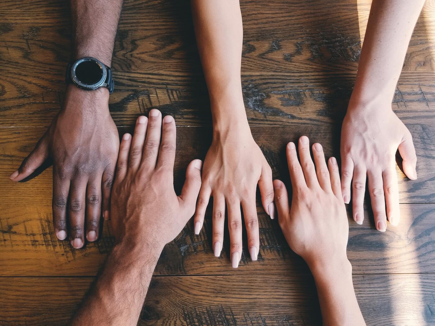 Five hands of different skin colors on a table 